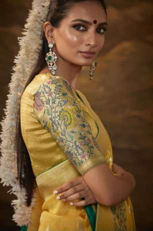 Woman wearing a yellow saree with intricate patterns against a warm-toned background
