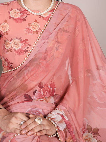 Person wearing a pink saree with floral patterns and a pearl necklace.